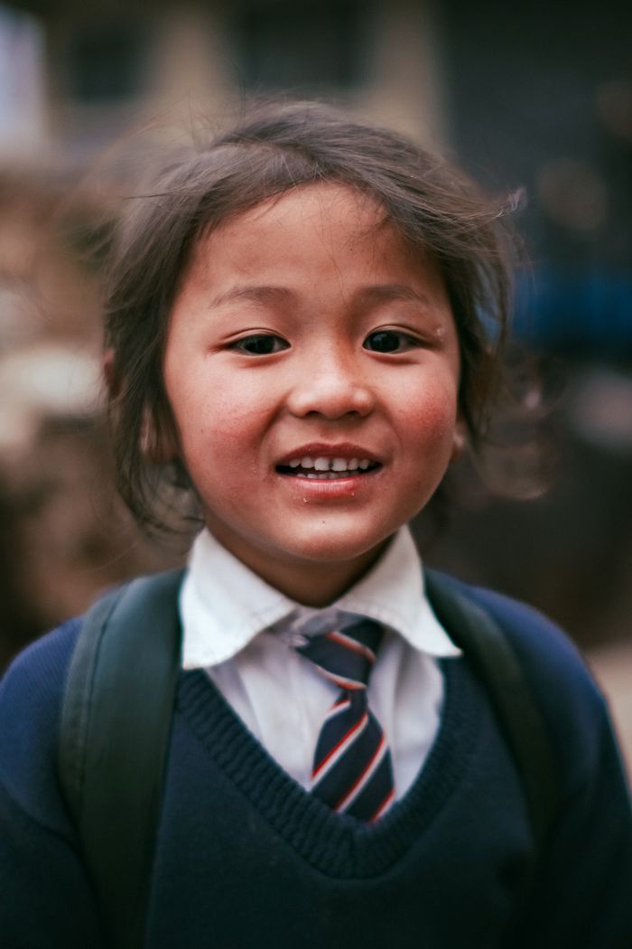 Portrait of a smiling Nepalese child in school uniform with backpack outdoors.
